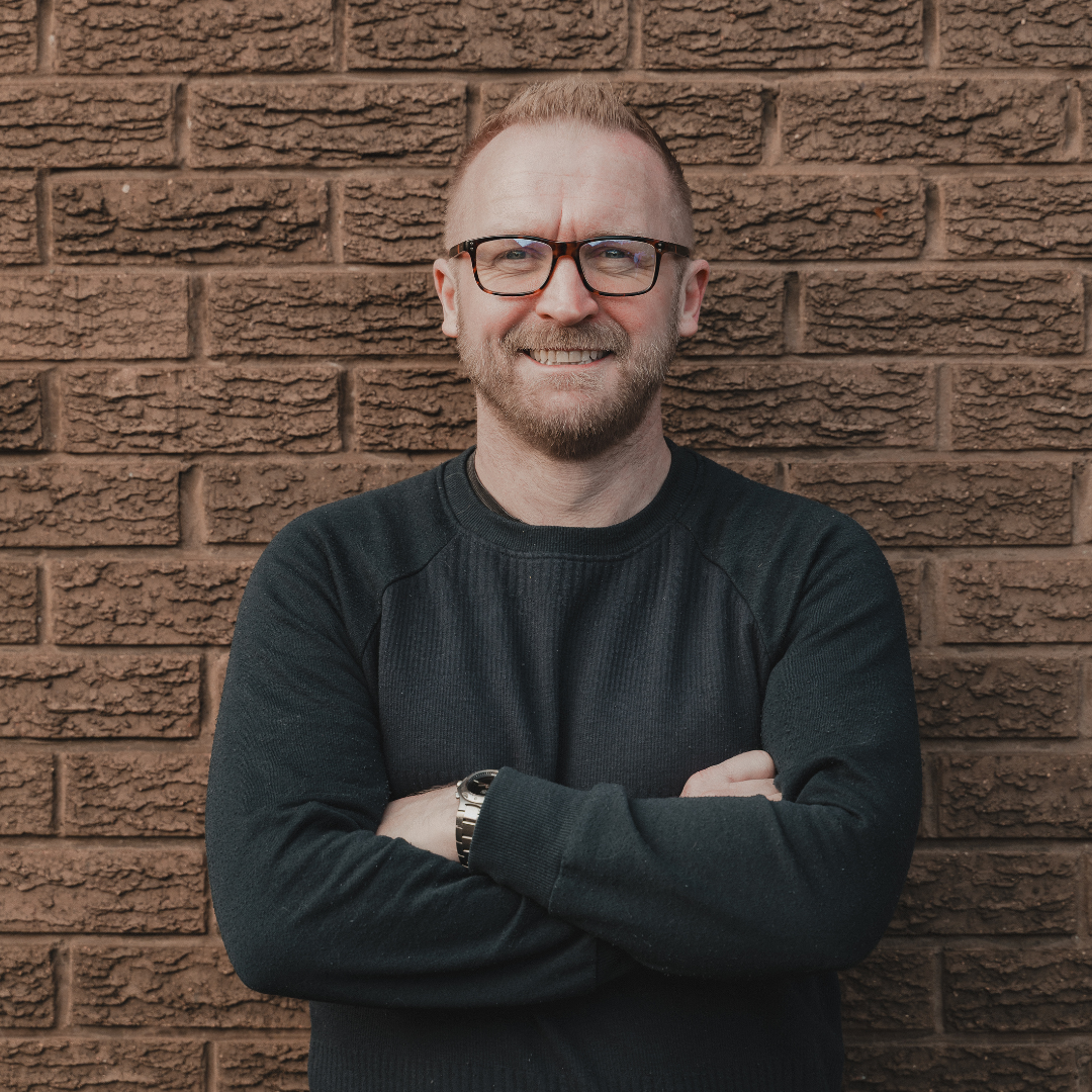 ZETA Press owner with glasses and a beard standing against a brick wall